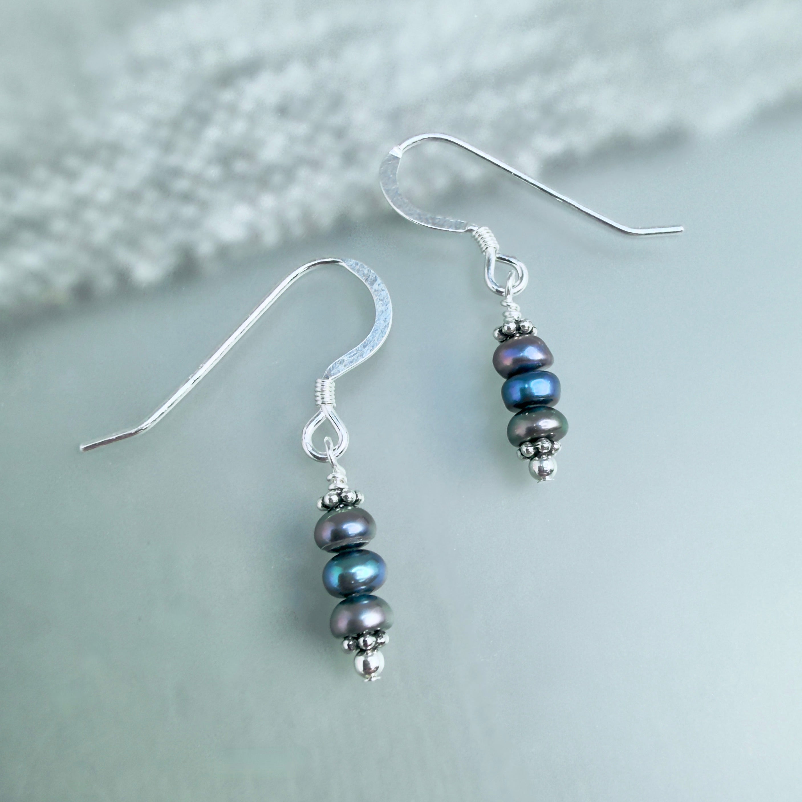 Pair of silver earrings with blue and gray pearl beads on a light gray background