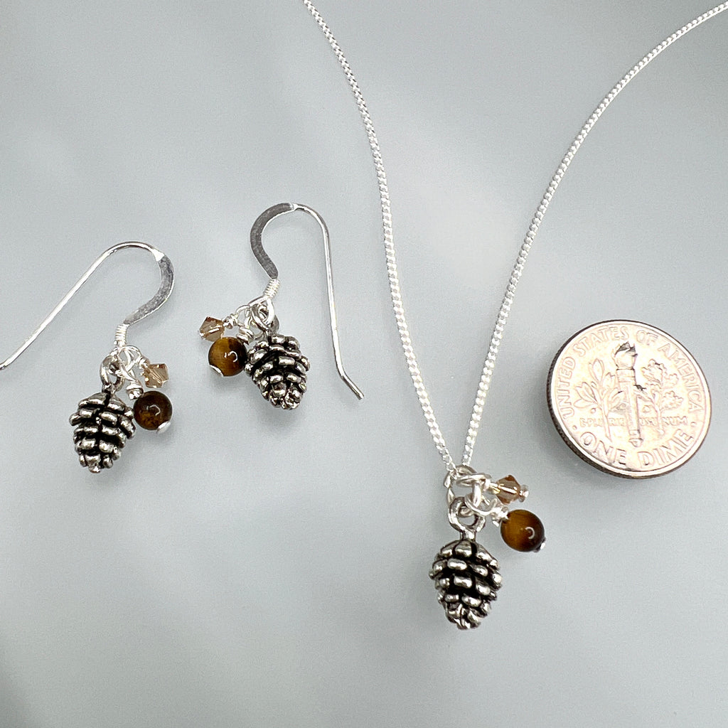Silver jewelry set with pinecone and bead charms on silver chain, next to a dime for scale on a gray background