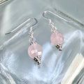 Pair of earrings with rose quartz and clear iridescent crystal beads and silver hooks on a clear glass surface