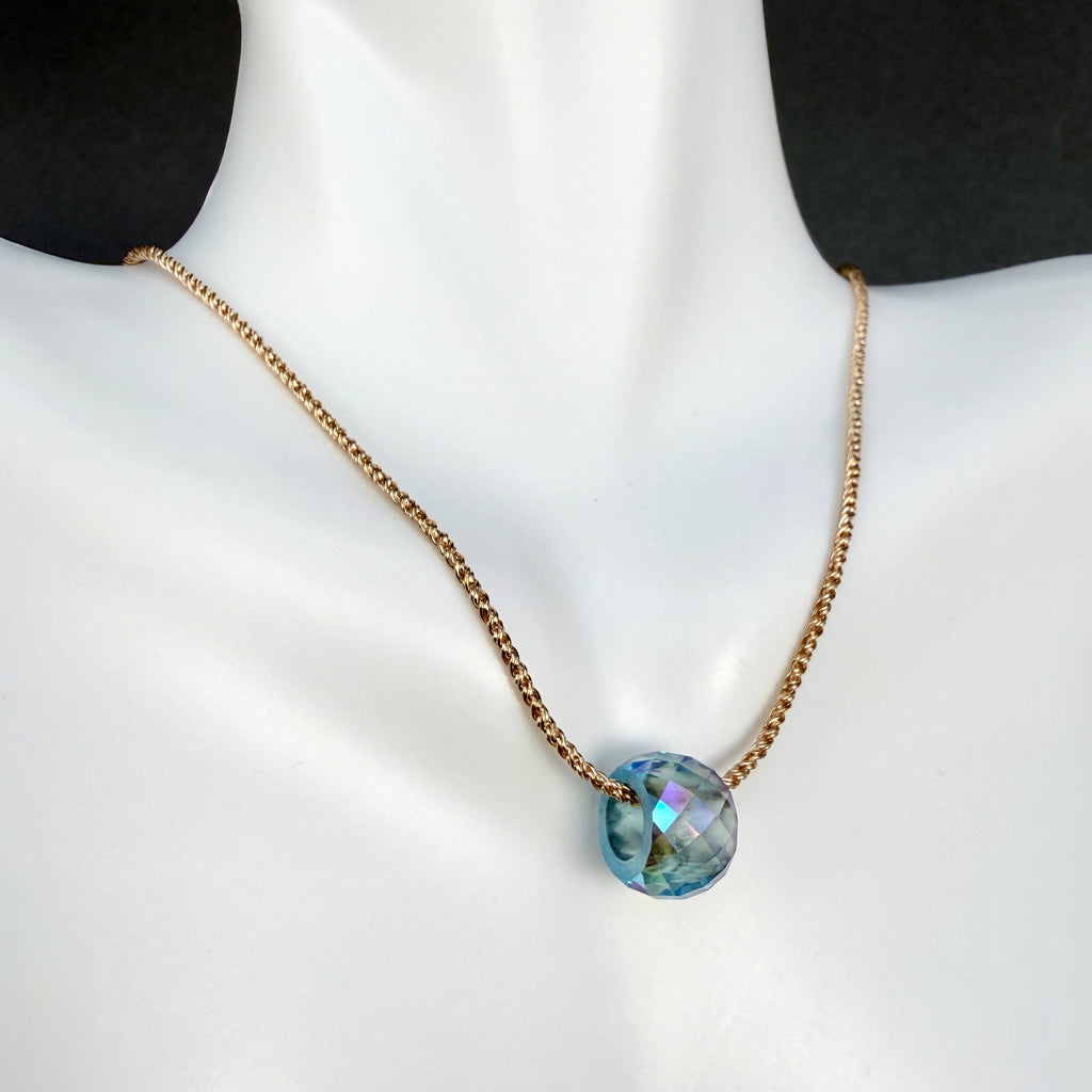 Gold chain necklace with a round faceted crystal, large hole bead pendant in pale blue/green with multi colored iridescent sheen, on a white mannequin