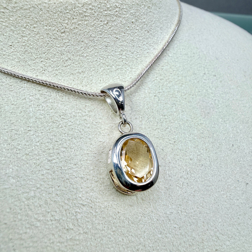 Silver pendant with a yellow gemstone on a light gray background