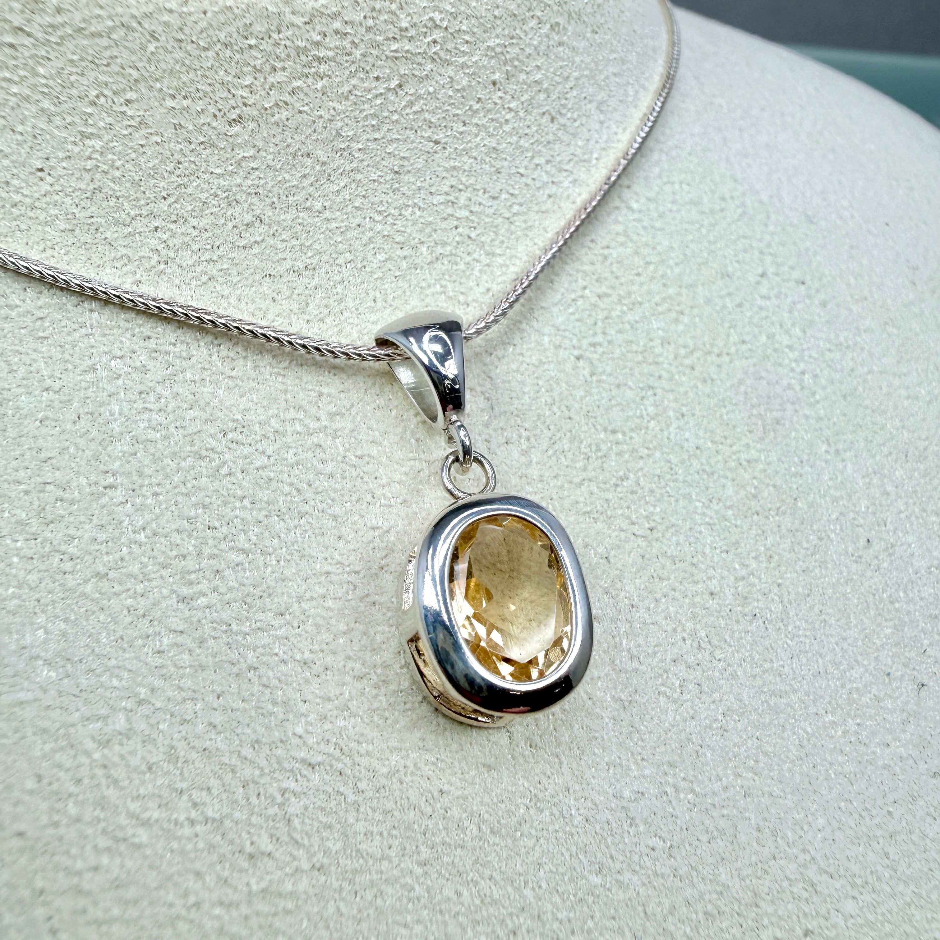 Silver pendant with a yellow gemstone on a light gray background