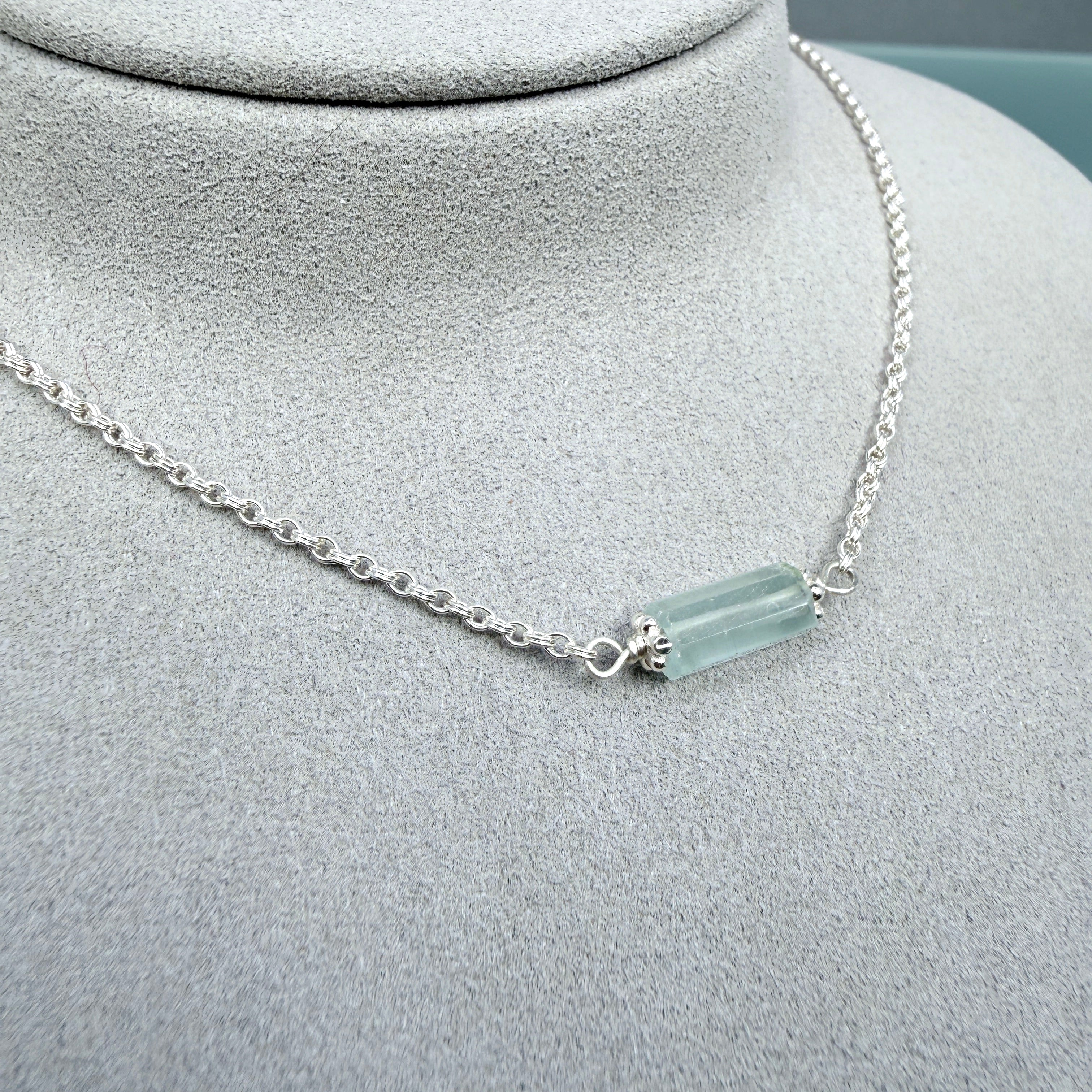 Necklace with a cylindrical pale Aquamarine gemstone on a gray mannequin bust