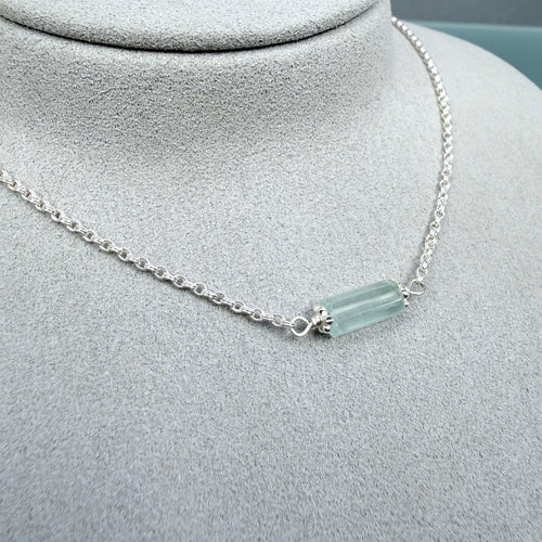 Necklace with a cylindrical pale Aquamarine gemstone on a gray mannequin bust