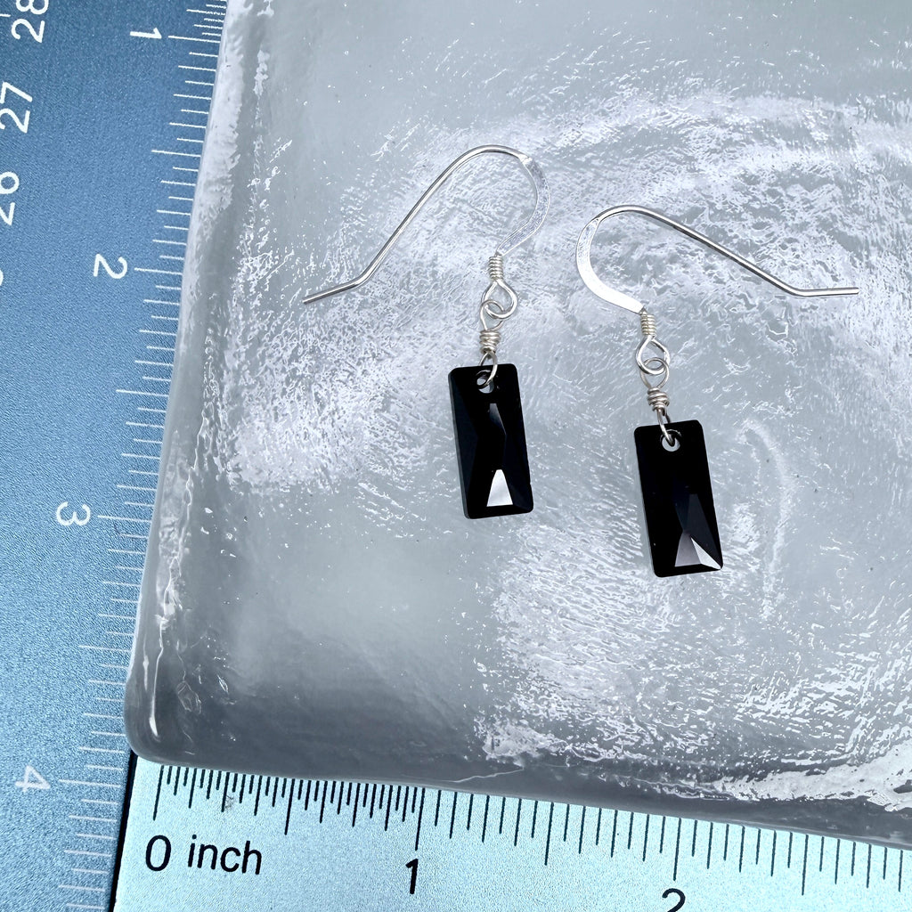 Black rectangular earrings on a clear stone surface with a ruler for scale.
