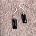 Black rectangular gemstone earrings on a textured beige/pink surface