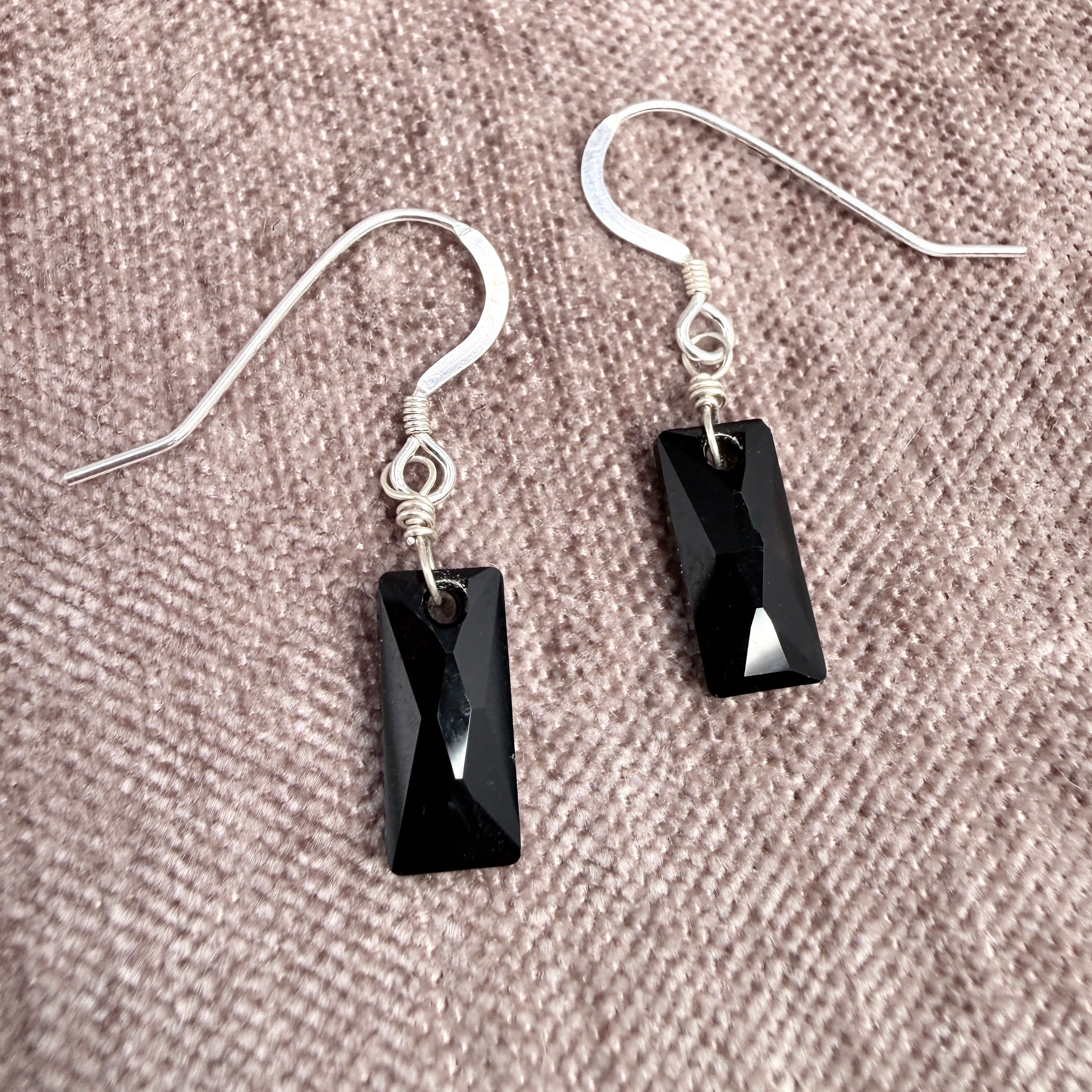 Black rectangular gemstone earrings on a textured beige/pink surface