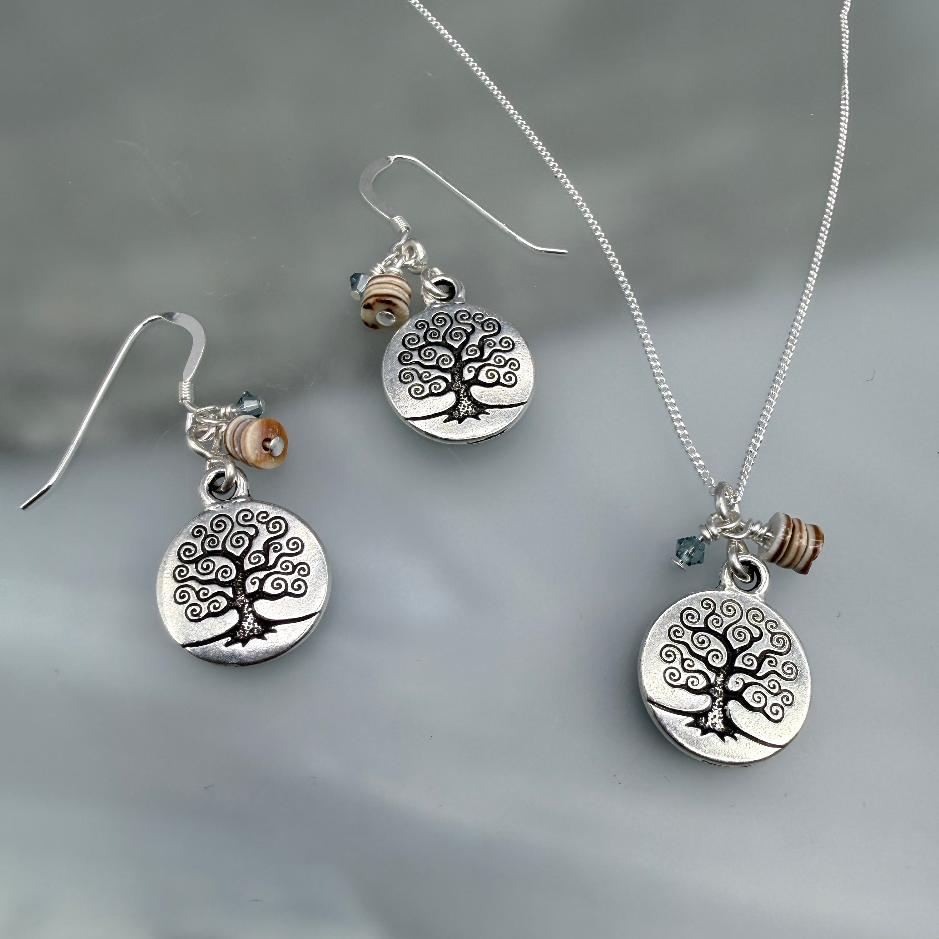 Silver jewelry set with tree-of-life charms on a gray background