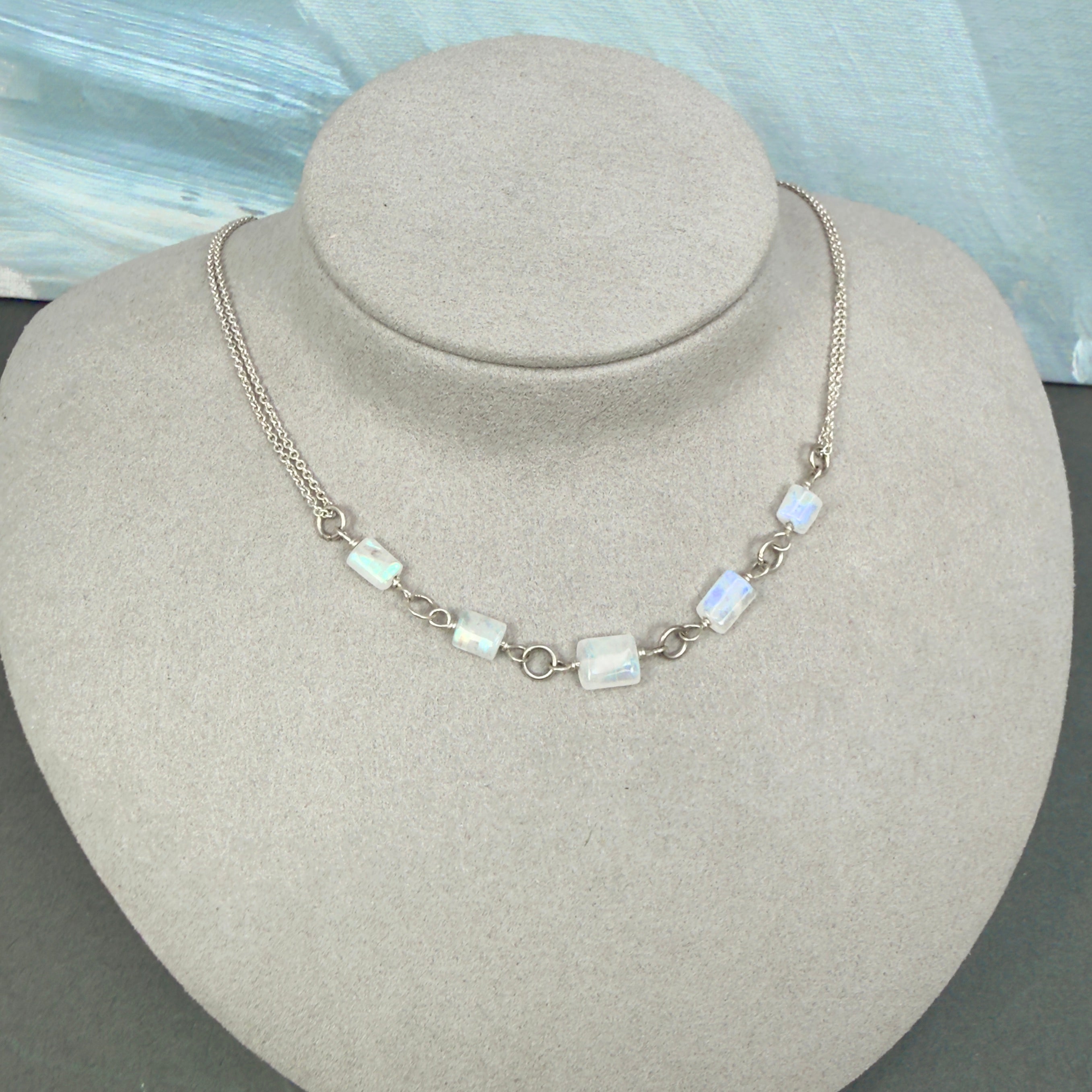 Necklace with rectangular rainbow moonstone beads on a gray bust