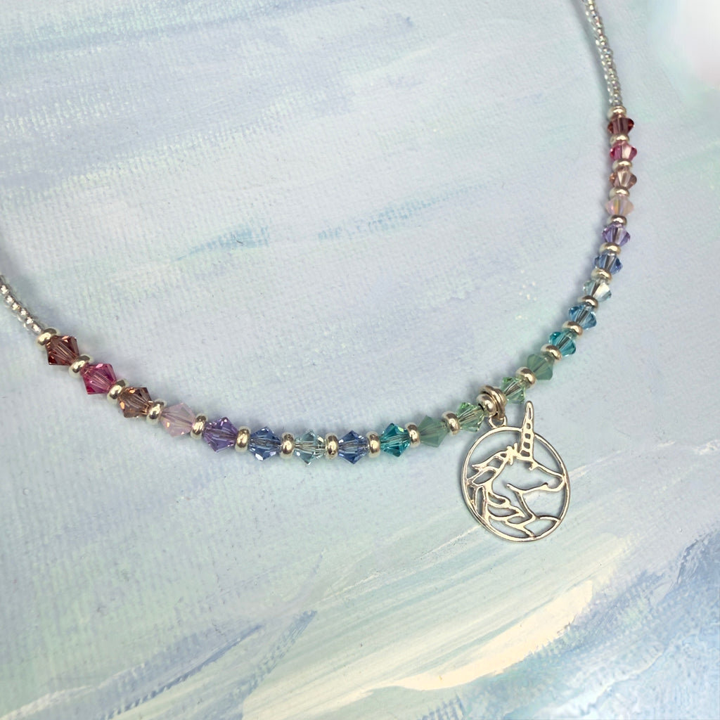 Necklace with multicolored pastel crystal beads and a silver unicorn pendant on a light blue textured background