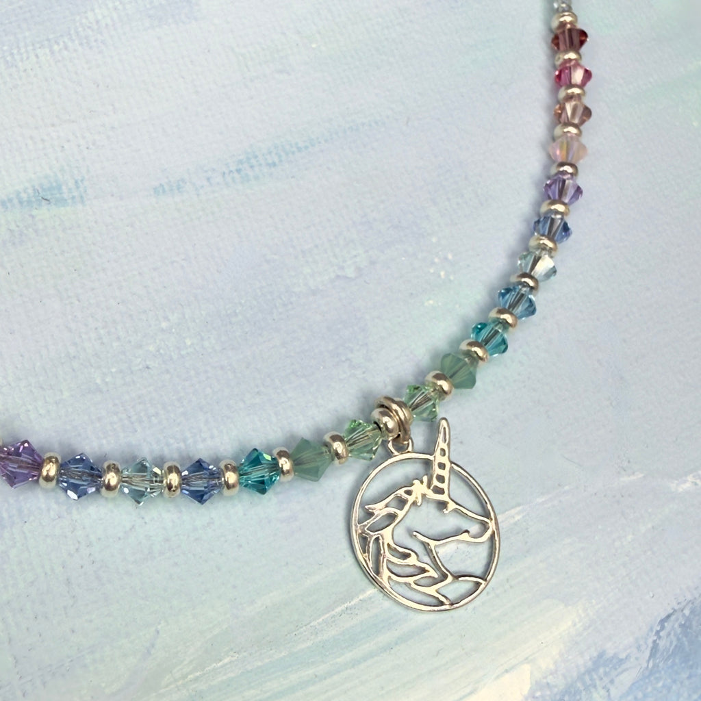 Necklace with colorful pastel beads and a unicorn charm on a light blue fabric background