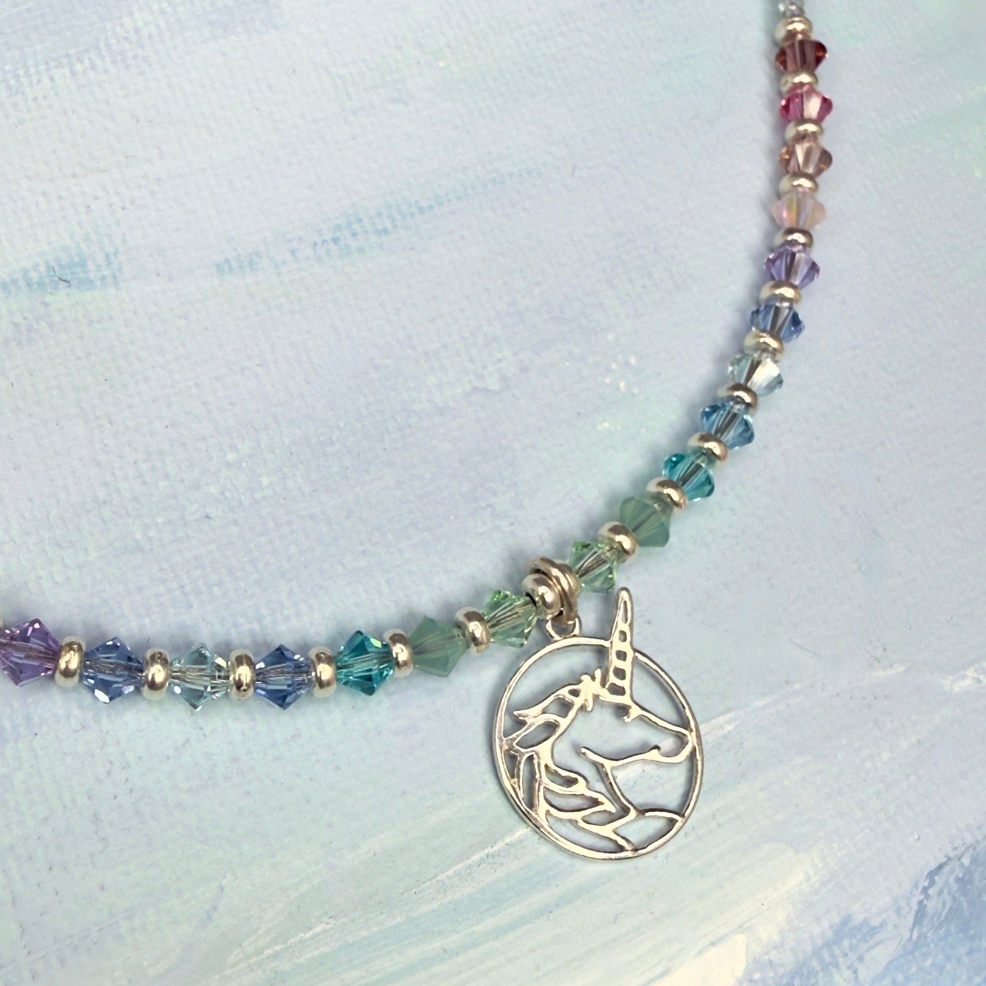 Necklace with colorful pastel beads and a unicorn charm on a light blue fabric background