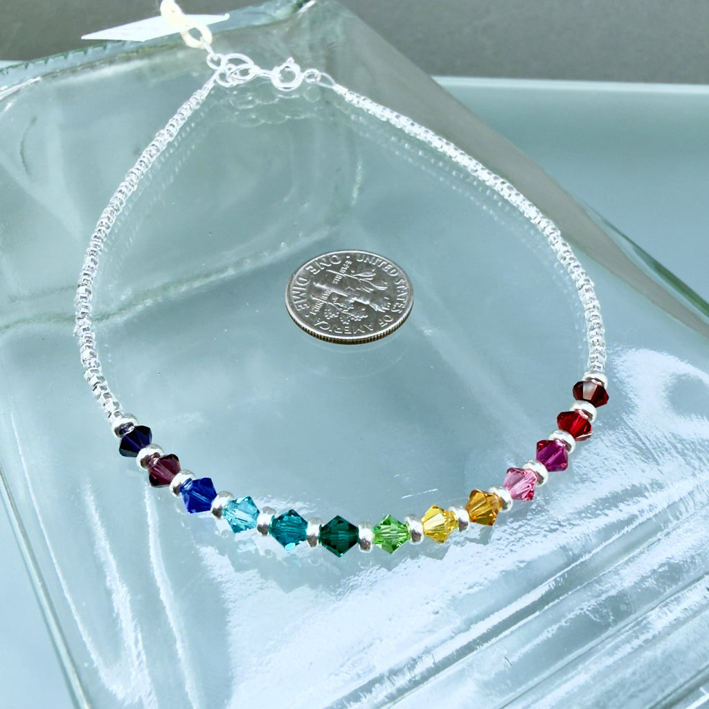 Multicolored beaded anklet on a clear glass surface with a coin for scale.