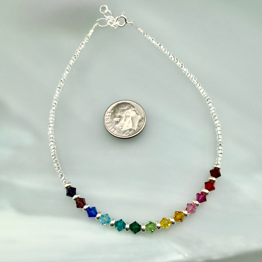 Anklet with multicolored beads next to a dime for scale on a light gray background