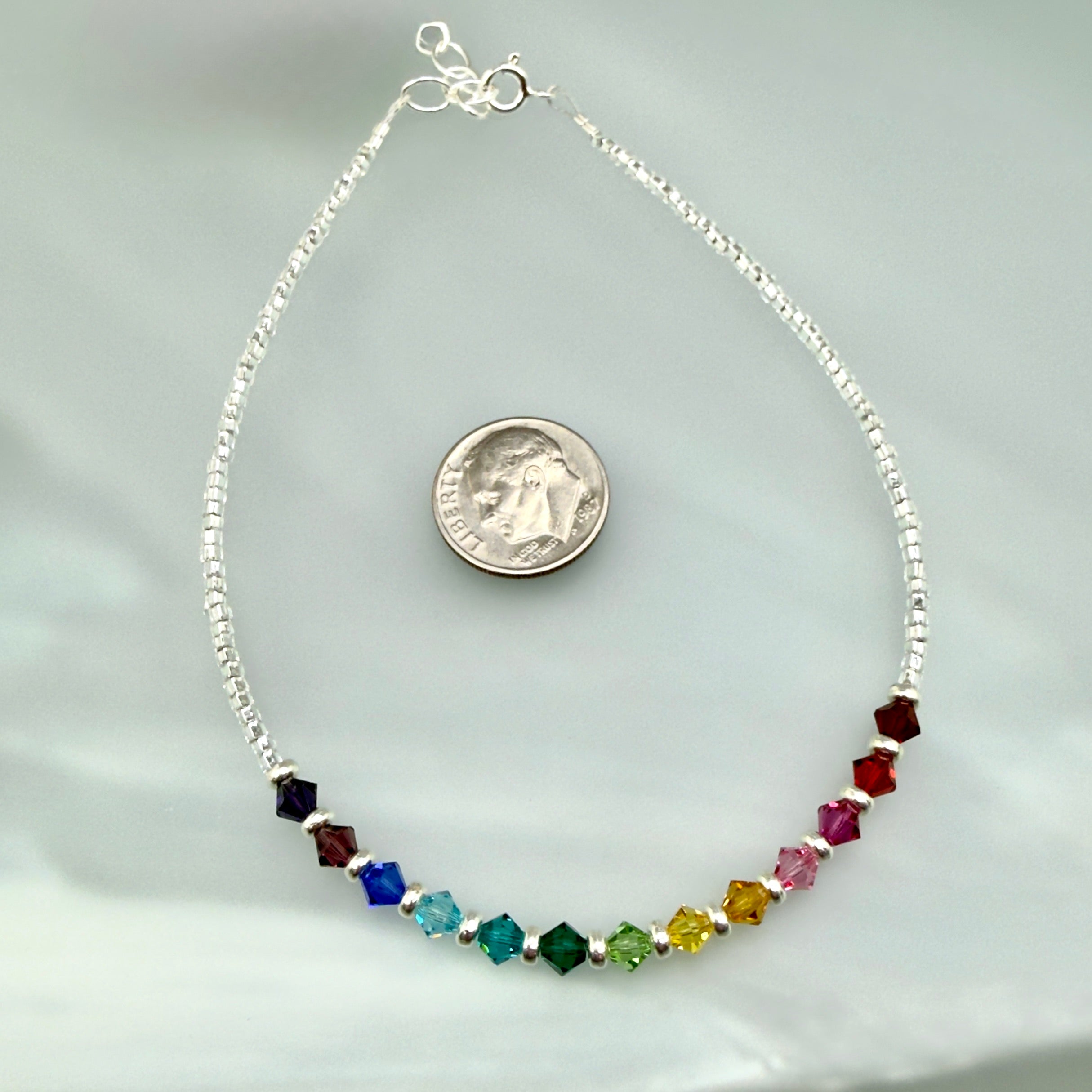 Anklet with multicolored beads next to a dime for scale on a light gray background