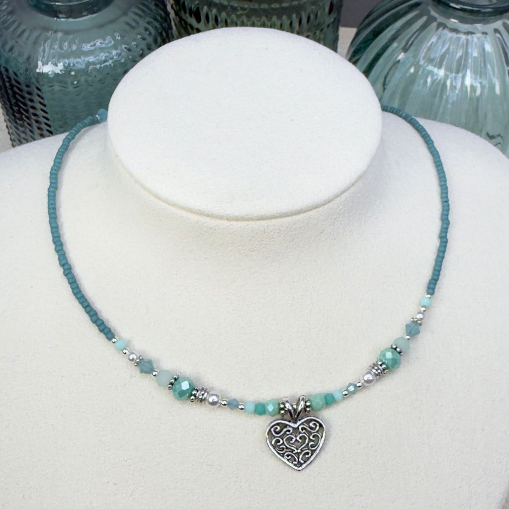 Soft minty green and white with silver accents and a heart pendant on an ivory mannequin bust against a neutral background with green glass bottles