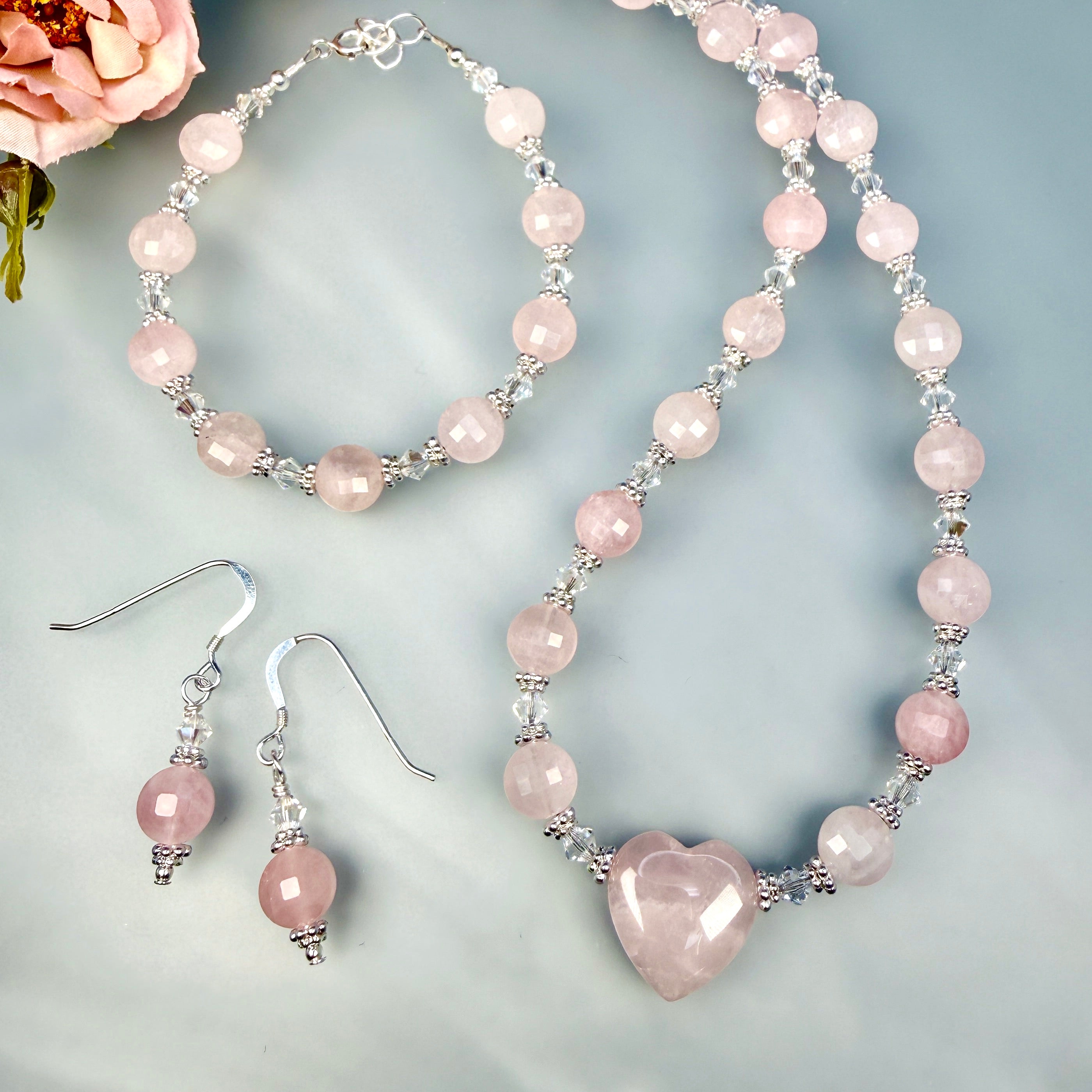 Necklace and earrings with pink heart-shaped beads on a light gray background
