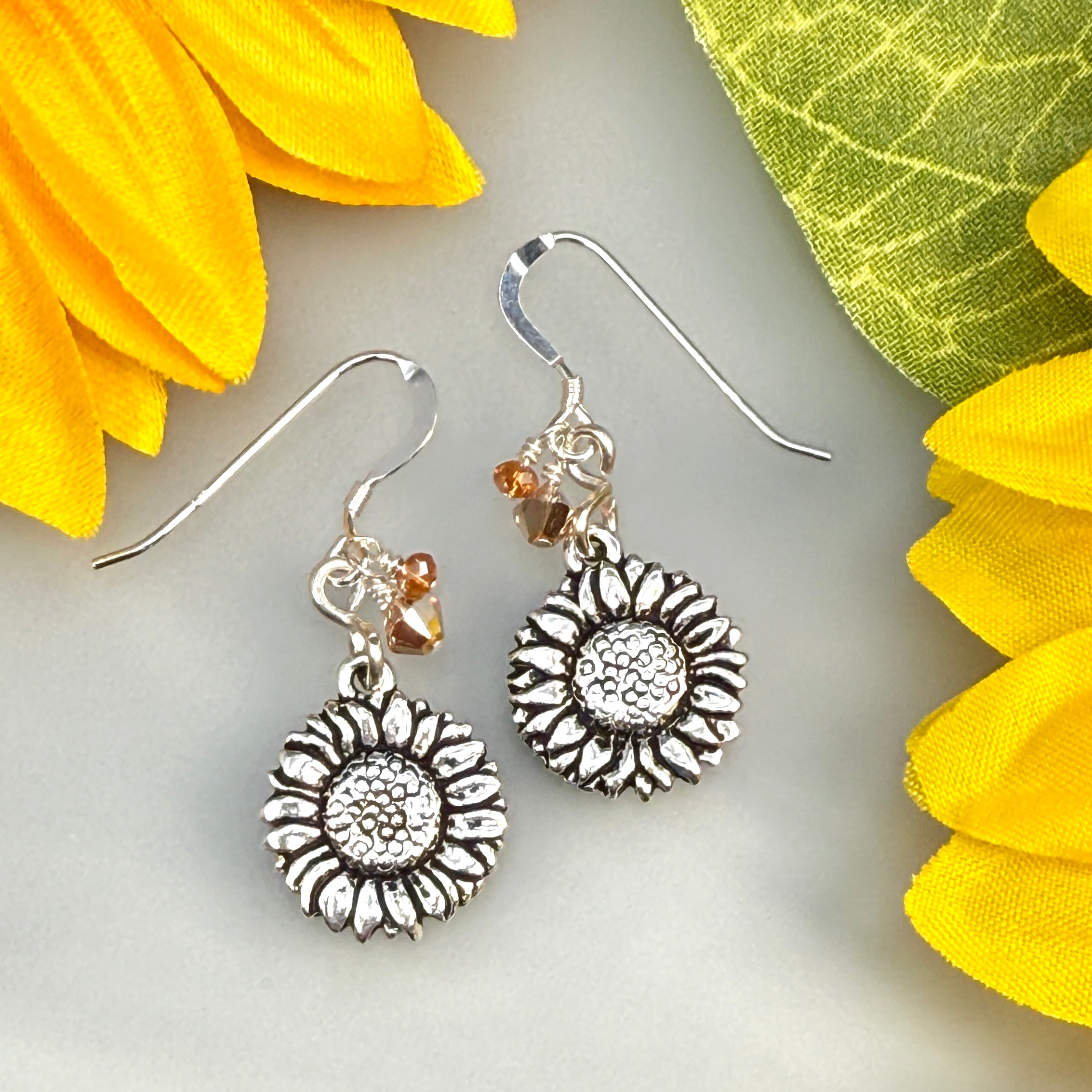 Silver sunflower earrings with small beads on a light gray background with yellow flowers.
