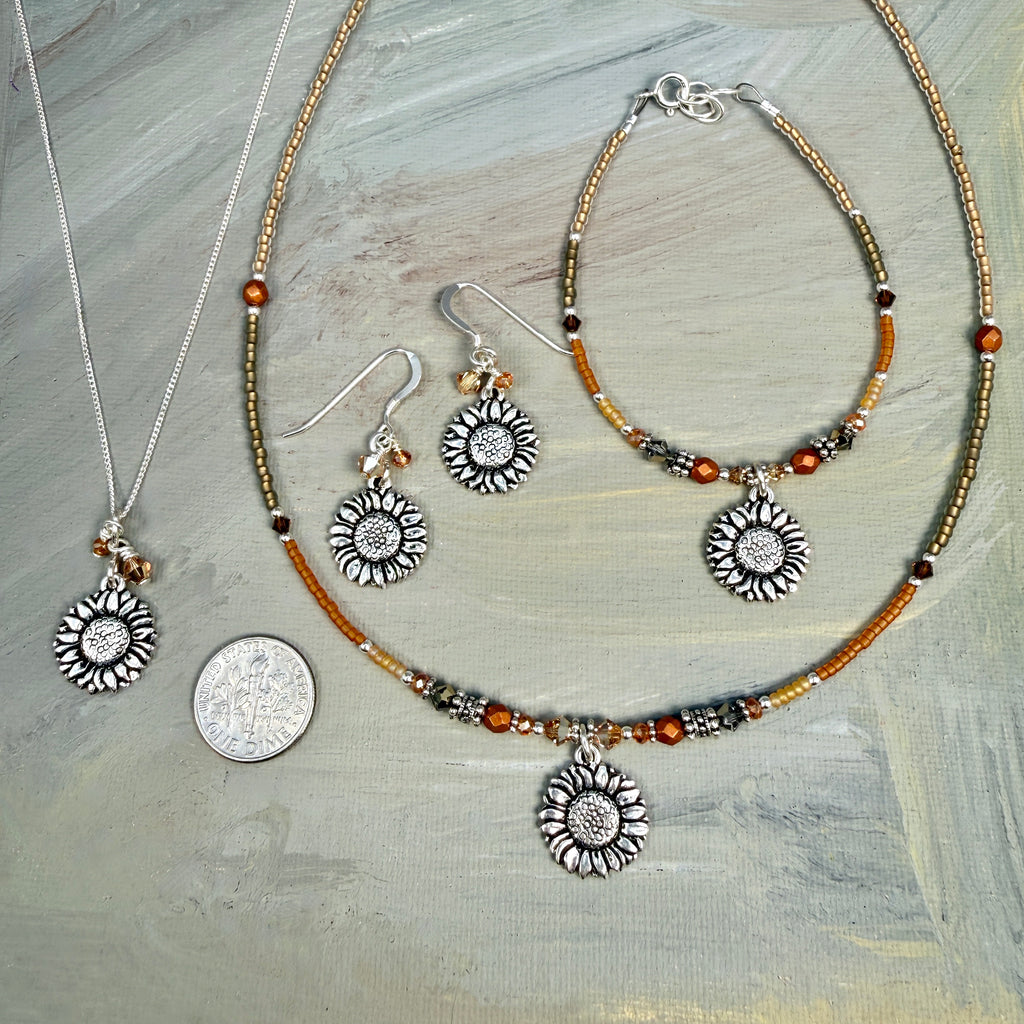 Jewelry set with sunflower-themed pendants on a textured surface, picture shows a dime for size comparison, sunflower charms are smaller than the dime