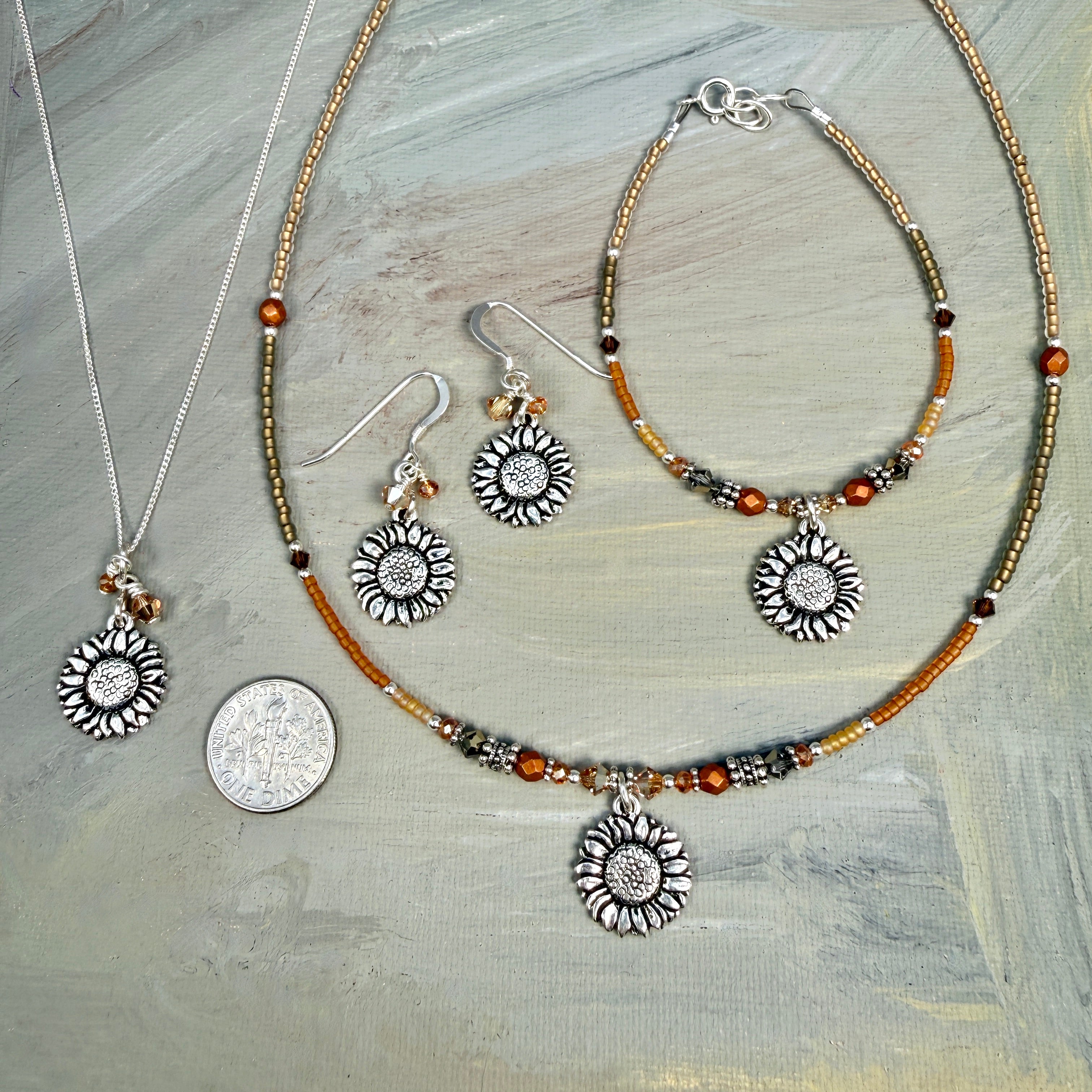 Jewelry set with sunflower-themed pendants on a textured surface, picture shows a dime for size comparison, sunflower charms are smaller than the dime