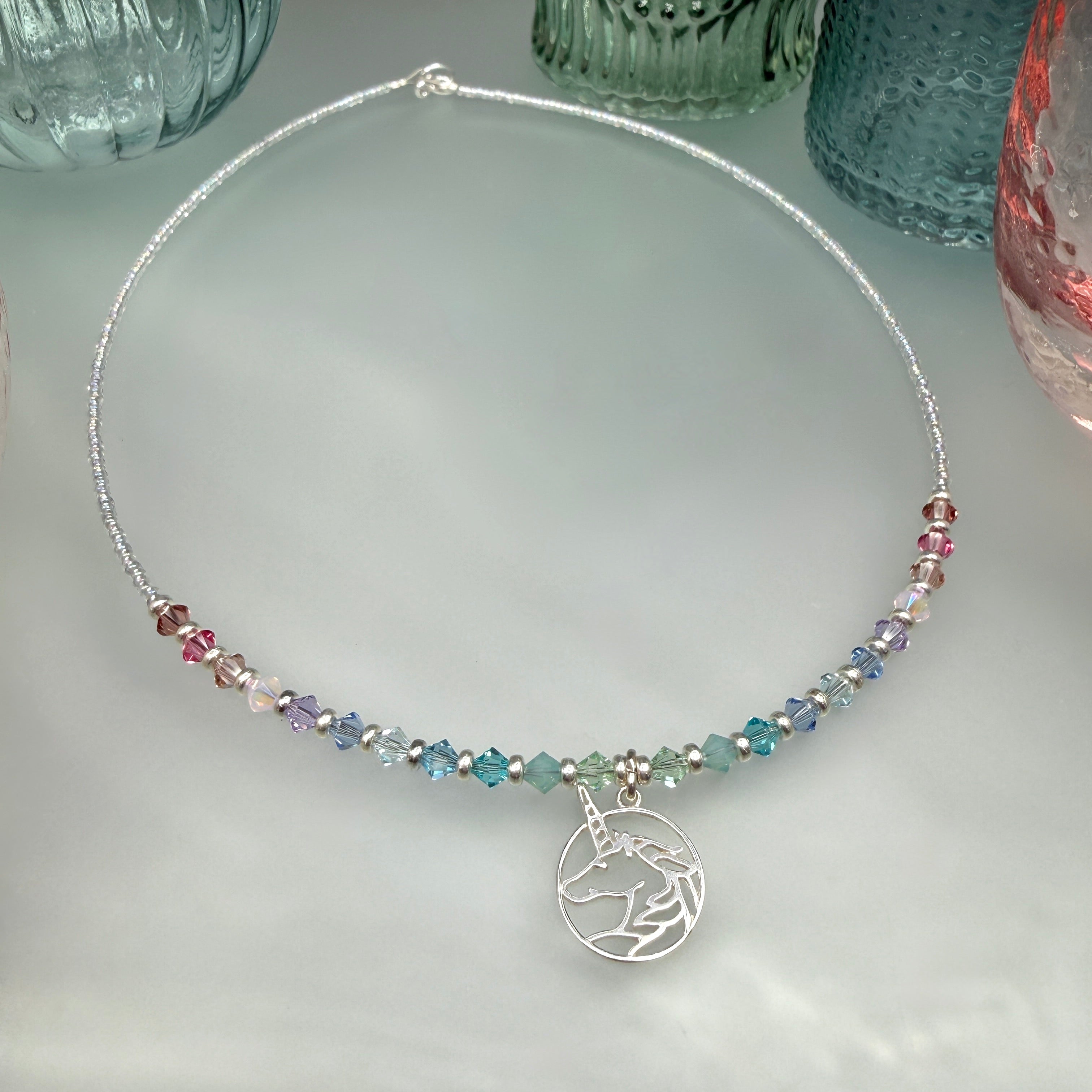 Necklace with multicolored pastel crystal beads and a unicorn charm on a light gray surface.