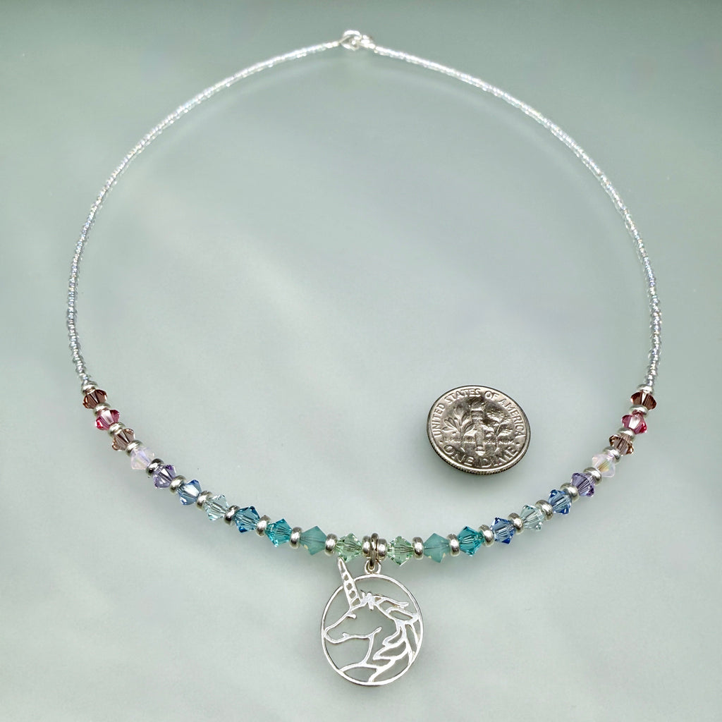 Necklace with unicorn charm and multicolored pastel beads on a light gray background, with a dime to demonstrate size. The unicorn pendant is just slightly larger than the dime.