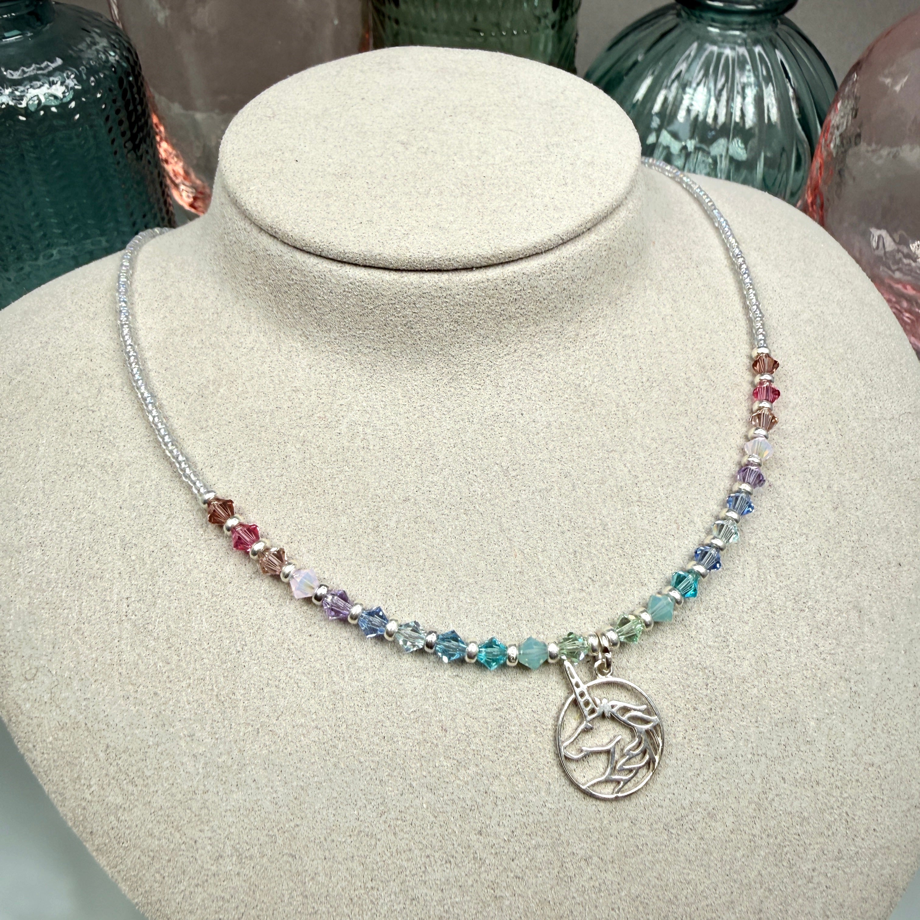 Multicolored pastel beaded necklace with a silver unicorn pendant on a mannequin bust.