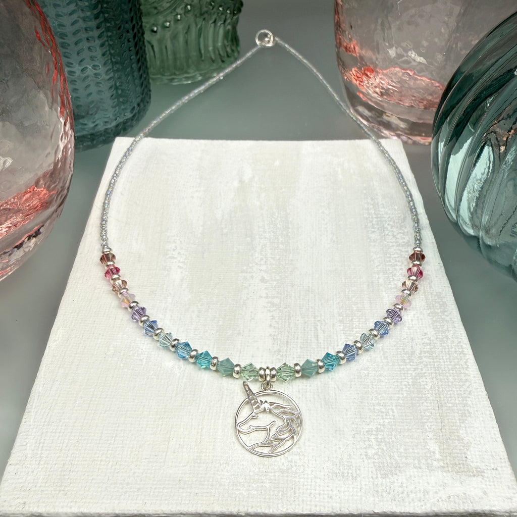 Necklace with multicolored pastel crystal beads and a silver unicorn pendant on a textured white background