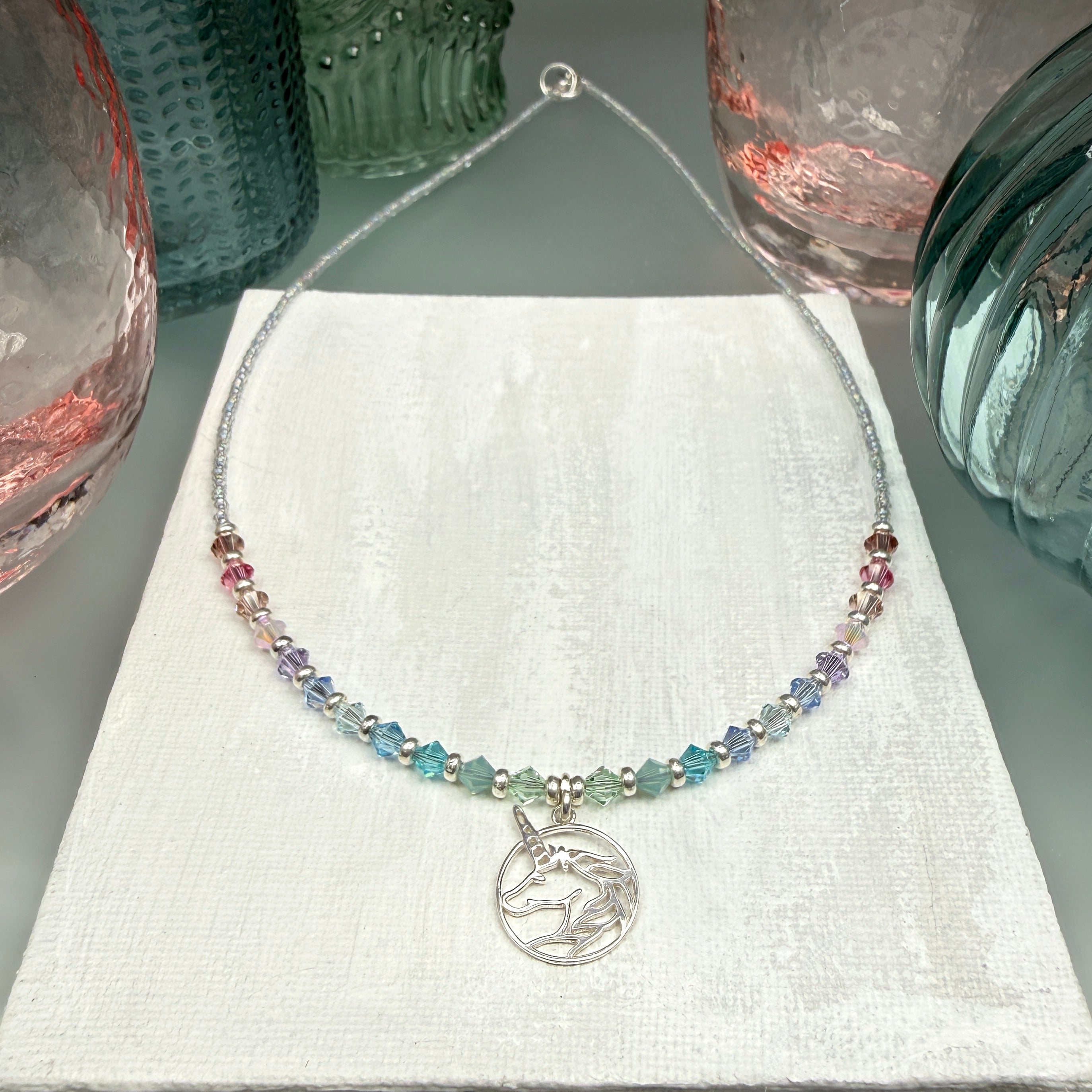 Necklace with multicolored pastel crystal beads and a silver unicorn pendant on a textured white background