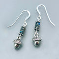 Grey and silver earrings on a pale grey background. The earrings feature a stack of natural grey labradorite gemstone with flashes of blue iridescence, with small silver pewter acorns beneath.
