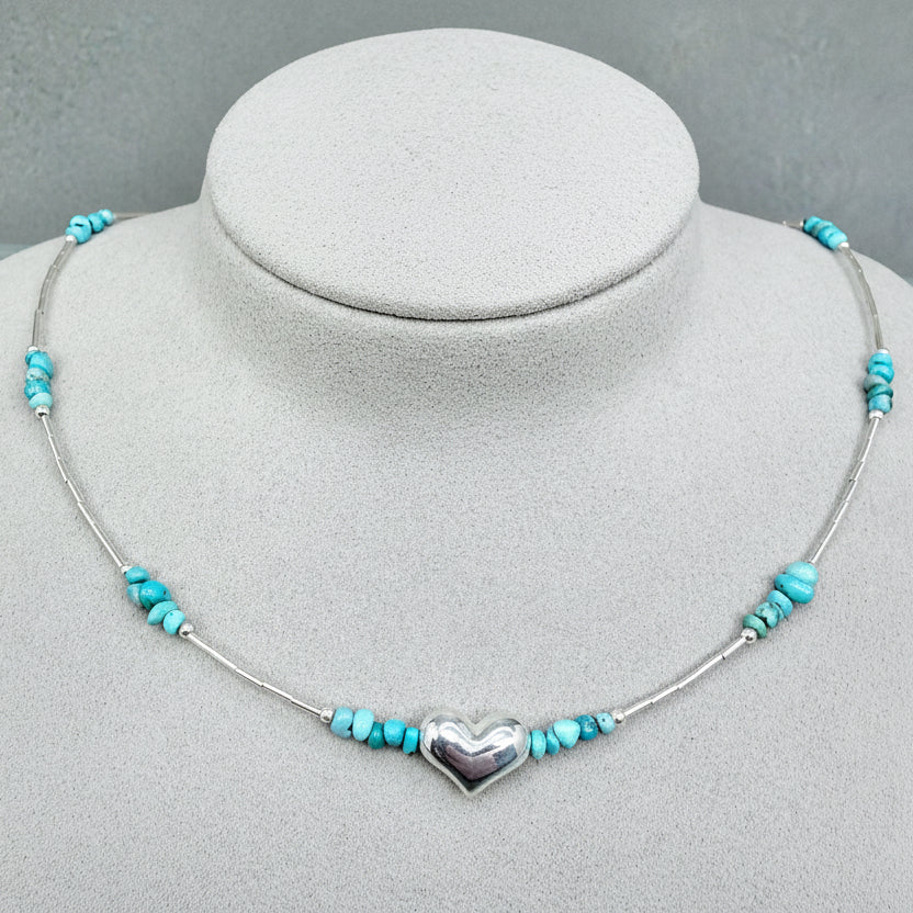 Turquoise beaded necklace with silver heart pendant on a gray mannequin bust.